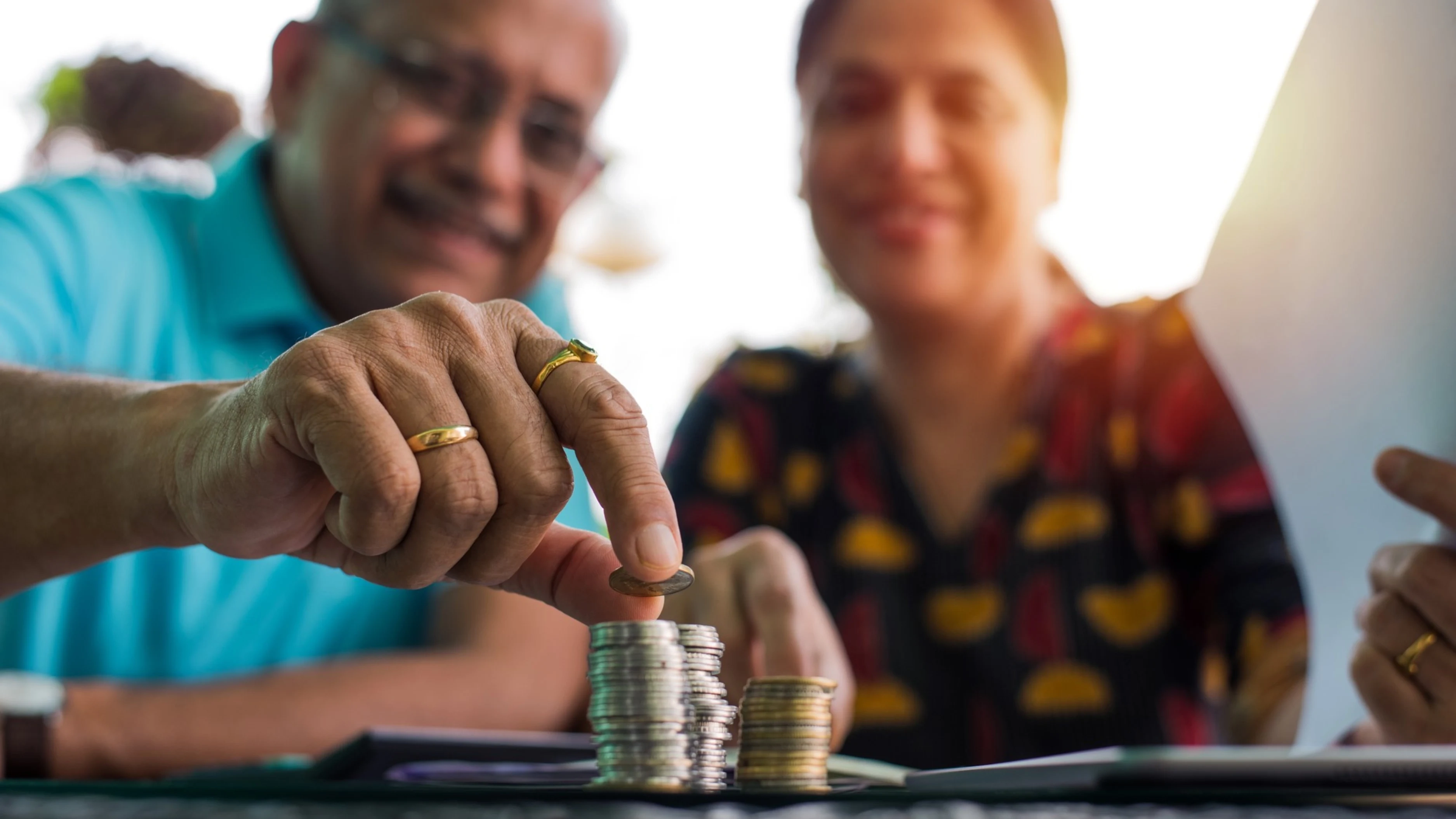 Um casal sorridente empilha moedas sobre a mesa, simbolizando planejamento e segurança financeira por meio do depósito do FGTS